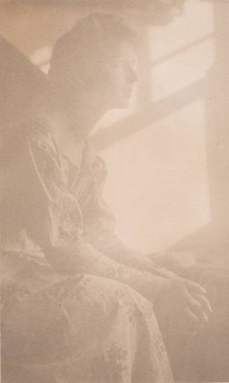 Woman in Flowered Dress Sitting With Hands Clasped in Lap