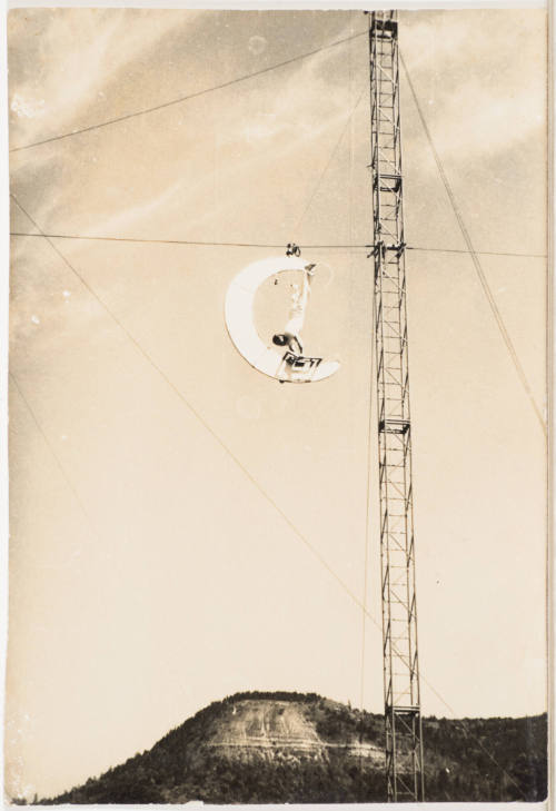 [Acrobat Dangling Upside Down on Crescent Moon Attached to Wire]