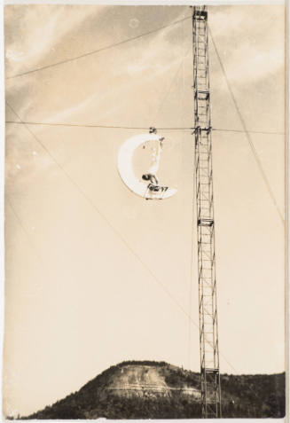 [Acrobat Dangling Upside Down on Crescent Moon Attached to Wire]